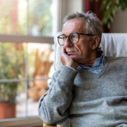Older man looking outside the window of his home.