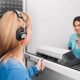 audiologist doing hearing exam to a mature patient using audiometer in special audio room.