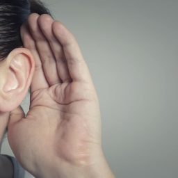 Woman cupping her ear with hear hand to try and hear better.