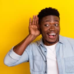 Happy man on yellow background holding his hand to his ear