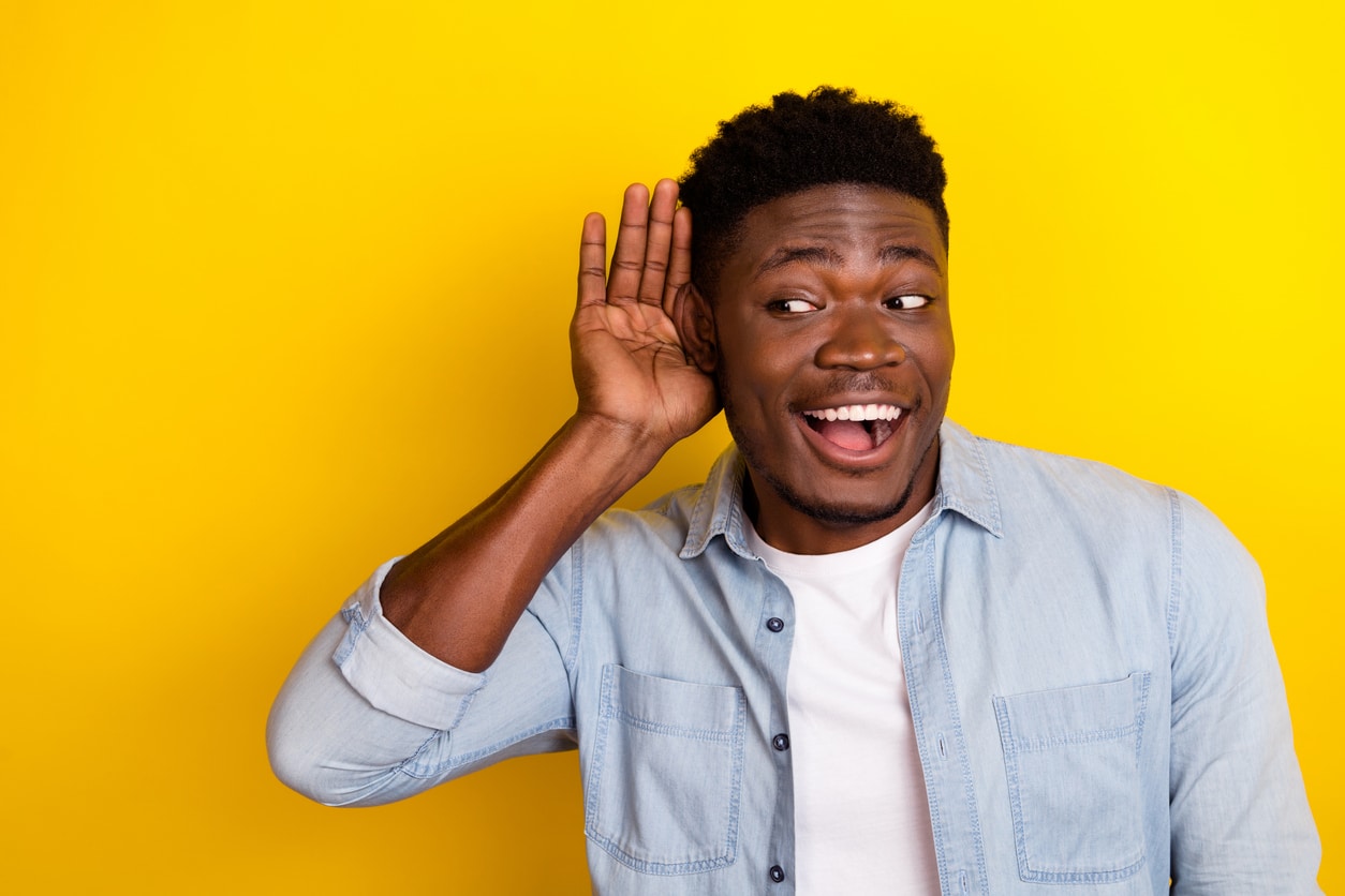 Happy man on yellow background holding his hand to his ear.