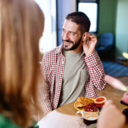 Smiling man wearing hearing aids while sitting at the kitchen table and talking with his family