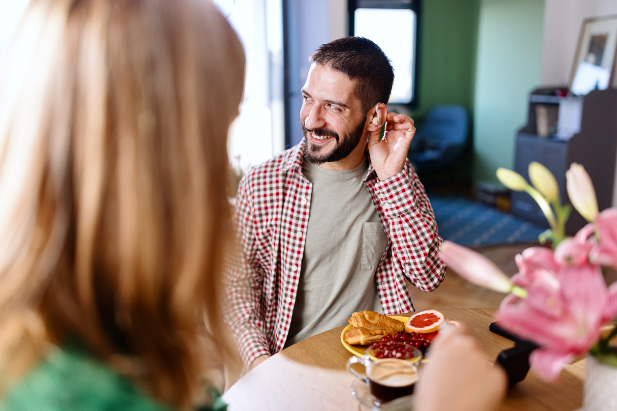 Smiling man wearing hearing aids while sitting at the kitchen table and talking with his family