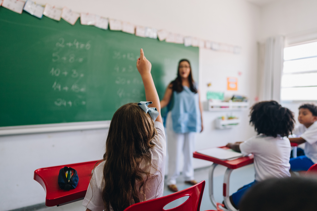 Rear view of a girl student raising her hand to ask on classroom at school