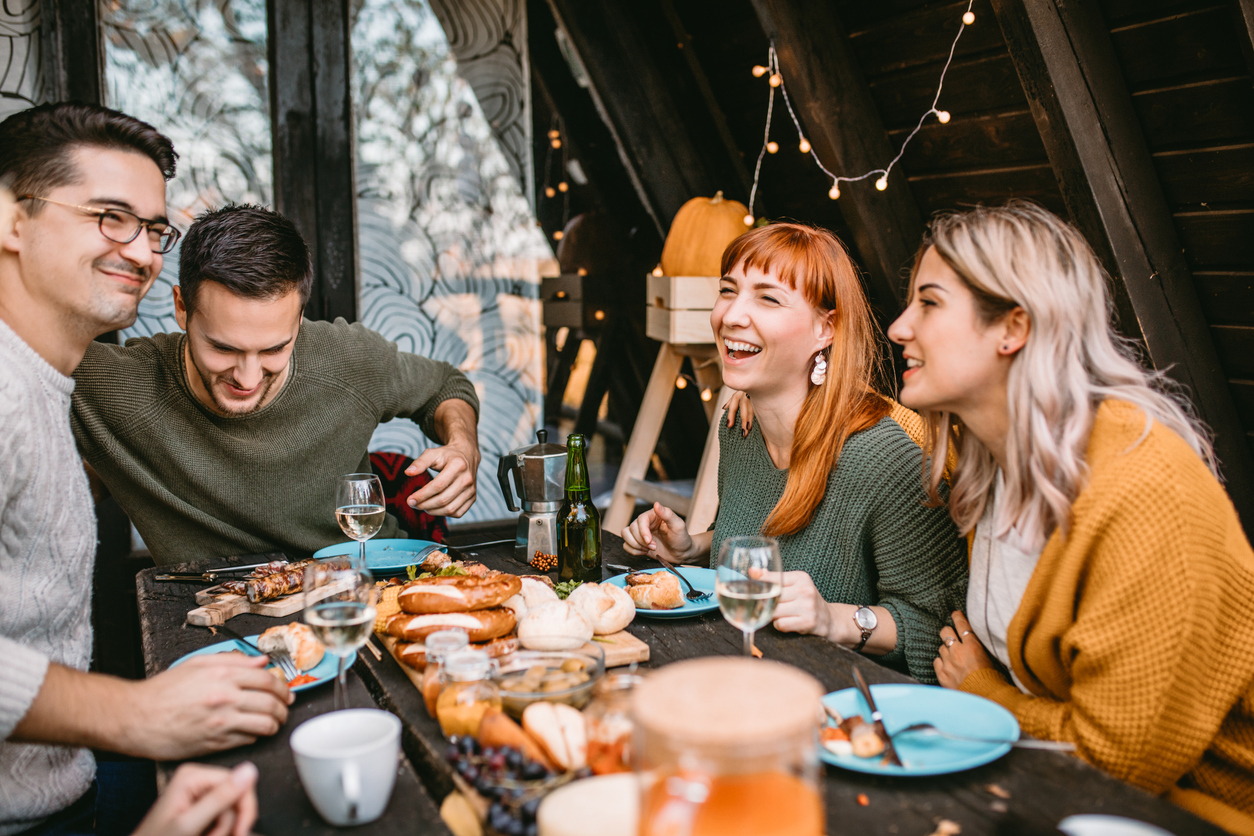 Group of smiling friends enjoys food and conversation at autumn picnic at weekend house