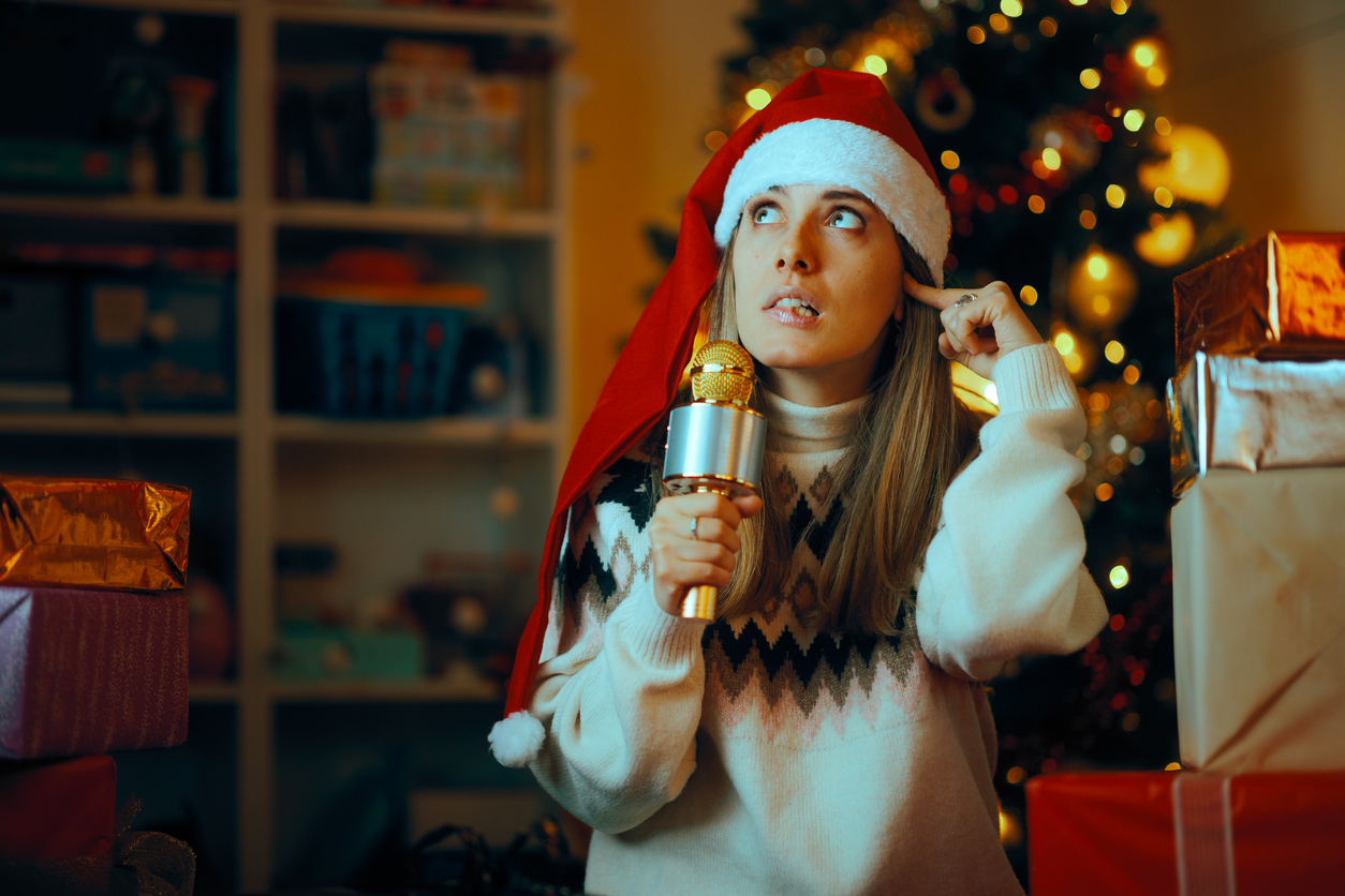 Woman in a santa hat surrounded by presents plugging her ears from noise.