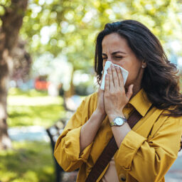 Woman with pollen allergies sneezing in the park.
