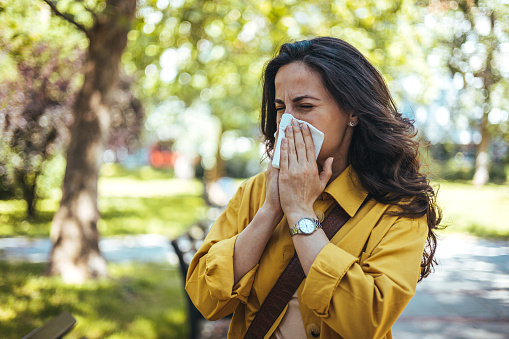Woman with pollen allergies sneezing in the park.
